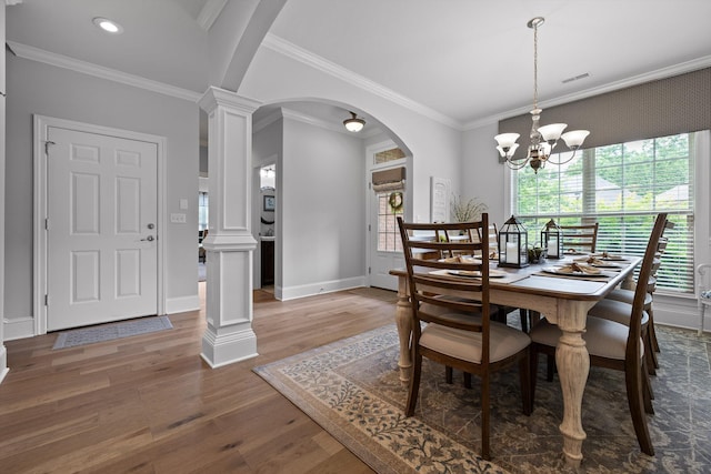 dining area featuring decorative columns, arched walkways, wood finished floors, crown molding, and a chandelier