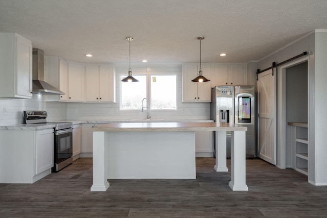kitchen with stainless steel appliances, wall chimney exhaust hood, a barn door, white cabinets, and light countertops