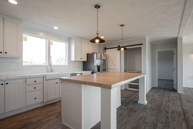 kitchen featuring stainless steel fridge with ice dispenser, a barn door, a sink, dark wood finished floors, and white cabinets