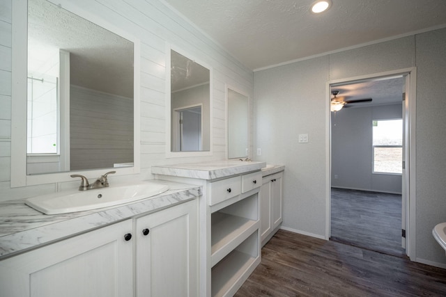 full bath with a textured ceiling, ornamental molding, wood finished floors, two vanities, and a ceiling fan