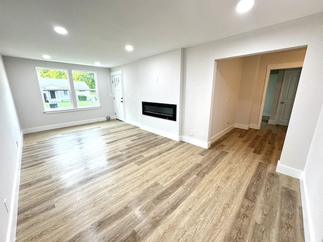 unfurnished living room with wood finished floors, a glass covered fireplace, recessed lighting, and baseboards