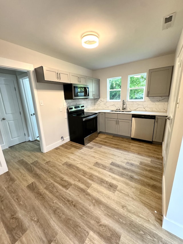 kitchen featuring appliances with stainless steel finishes, a sink, gray cabinets, and backsplash