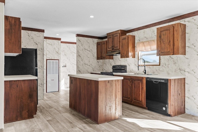kitchen with black appliances, a sink, under cabinet range hood, light wood-type flooring, and light countertops