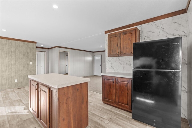 kitchen with freestanding refrigerator, ornamental molding, a kitchen island, light countertops, and light wood-style flooring