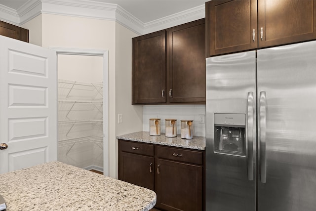 kitchen with stainless steel refrigerator with ice dispenser, dark brown cabinets, light stone counters, and crown molding