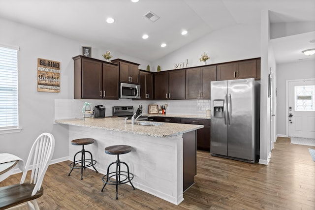 kitchen featuring stainless steel appliances, a sink, dark brown cabinetry, a peninsula, and decorative backsplash