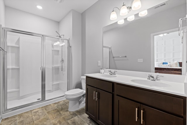ensuite bathroom featuring toilet, a stall shower, double vanity, and stone finish flooring