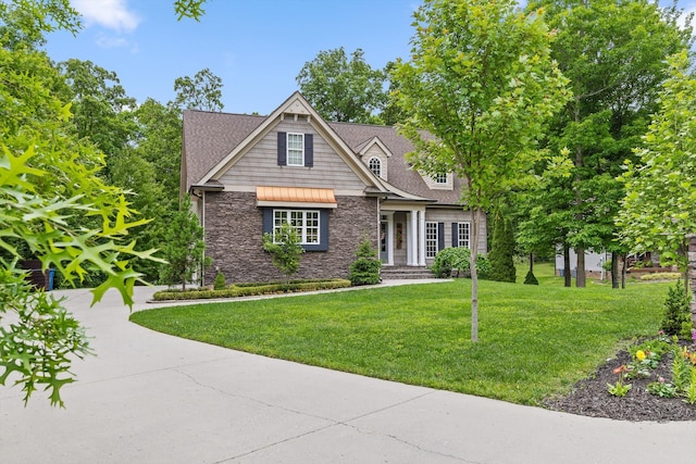 view of front facade featuring stone siding, a front yard, and roof with shingles