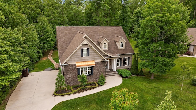 view of front of property featuring concrete driveway, a front yard, stone siding, and a shingled roof