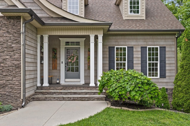 entrance to property with roof with shingles, a porch, and stone siding
