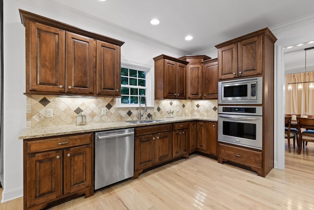 kitchen featuring appliances with stainless steel finishes, a sink, light wood finished floors, ornamental molding, and light stone counters