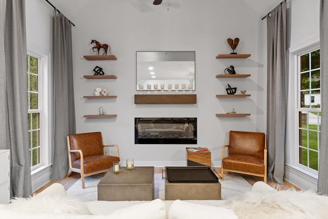 living room featuring wood finished floors, a glass covered fireplace, baseboards, and ceiling fan