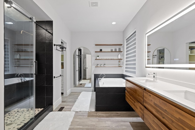 full bathroom with wood finished floors, a garden tub, a shower stall, double vanity, and recessed lighting