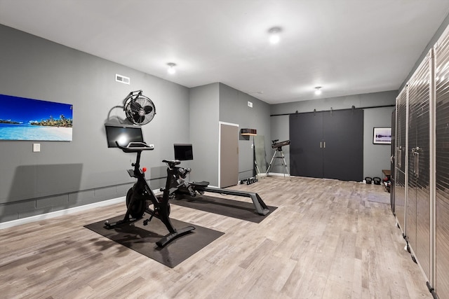 exercise area with a barn door, wood finished floors, and baseboards