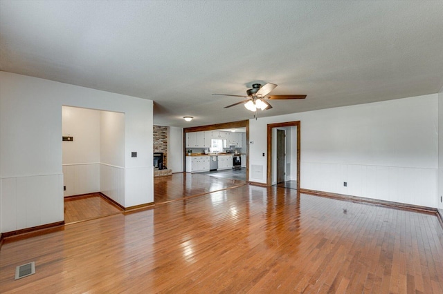 unfurnished living room featuring ceiling fan, light wood-style floors, wainscoting, and a fireplace