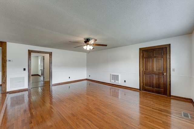 unfurnished room with wood finished floors, a textured ceiling, a ceiling fan, a wainscoted wall, and baseboards