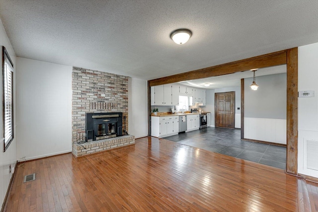 unfurnished living room featuring dark wood-style floors, a textured ceiling, a fireplace, a wainscoted wall, and a sink