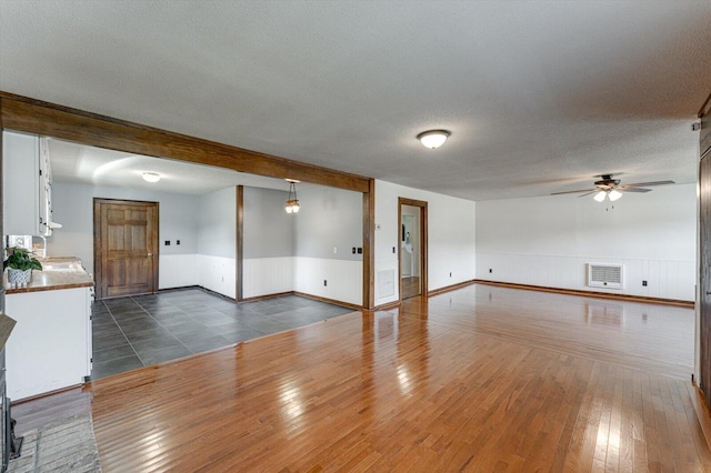 unfurnished living room featuring ceiling fan, a wainscoted wall, a textured ceiling, dark wood-style flooring, and a sink
