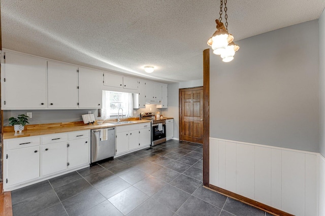 kitchen with stainless steel appliances, a sink, a textured ceiling, a wainscoted wall, and white cabinetry