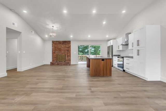 kitchen featuring lofted ceiling, appliances with stainless steel finishes, wall chimney exhaust hood, a kitchen island, and open floor plan
