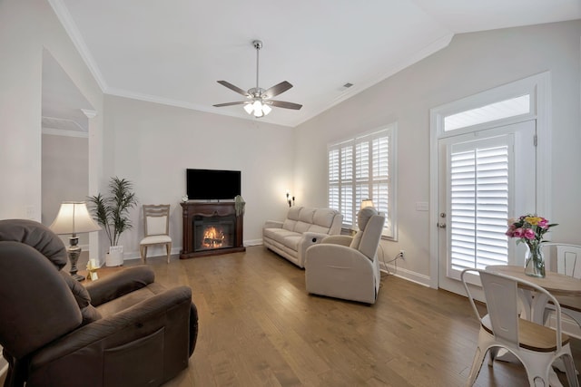living area with ceiling fan, light wood finished floors, a glass covered fireplace, baseboards, and crown molding