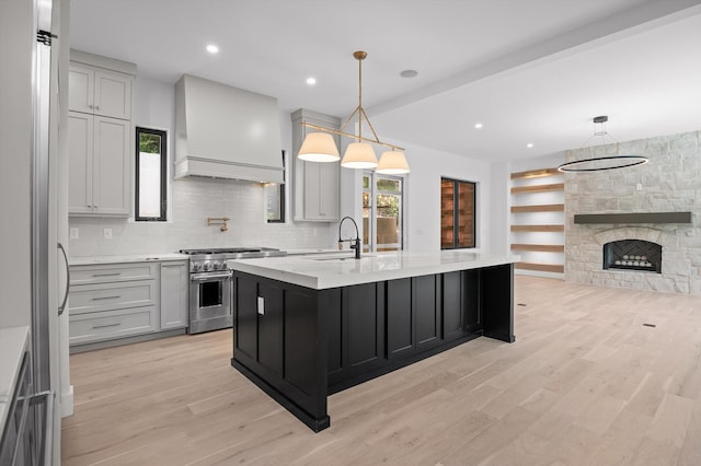 1608 Knickerbocker Ave, Chattanooga, TN 37405 - kitchen with stainless steel stove, wall chimney exhaust hood, a sink, light wood-style flooring, and a center island with sink