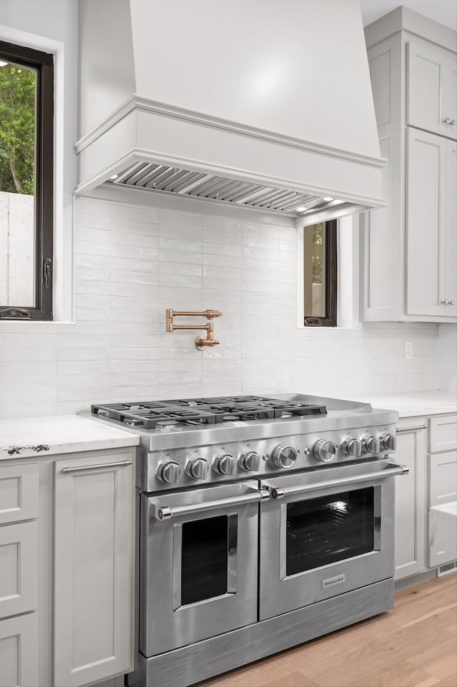 1608 Knickerbocker Ave, Chattanooga, TN 37405 - kitchen featuring range with two ovens, custom range hood, decorative backsplash, light stone countertops, and light wood finished floors