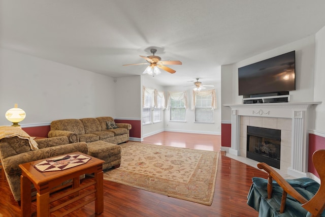 living room featuring a ceiling fan, a tiled fireplace, wood finished floors, and baseboards