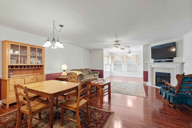 dining space with a ceiling fan, a tile fireplace, wood finished floors, and a chandelier