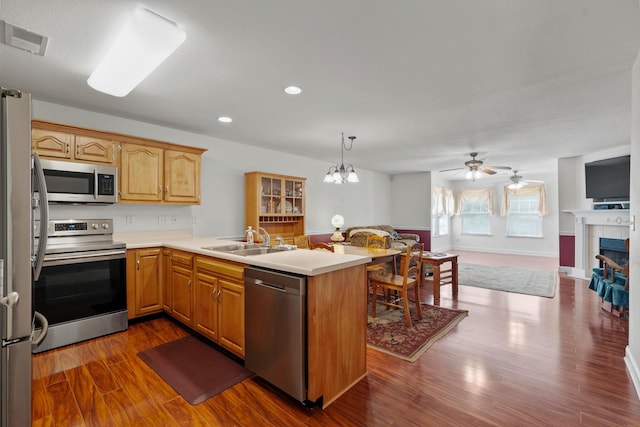 kitchen featuring stainless steel appliances, a sink, a peninsula, light countertops, and dark wood-style flooring