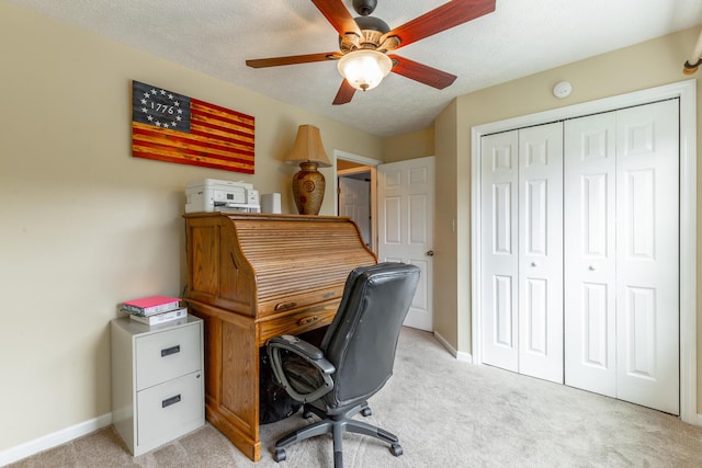 office space featuring light colored carpet, a ceiling fan, baseboards, and a textured ceiling