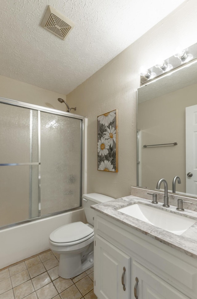 full bath with tile patterned flooring, combined bath / shower with glass door, a textured ceiling, vanity, and toilet