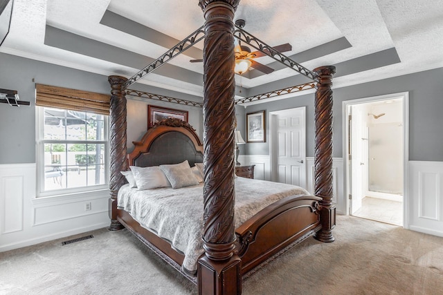 bedroom with a tray ceiling, carpet floors, a wainscoted wall, a textured ceiling, and connected bathroom