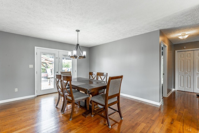 dining space with a textured ceiling, baseboards, wood-type flooring, and a chandelier