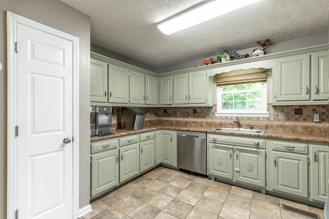 kitchen with stainless steel dishwasher, a sink, green cabinetry, a textured ceiling, and tasteful backsplash