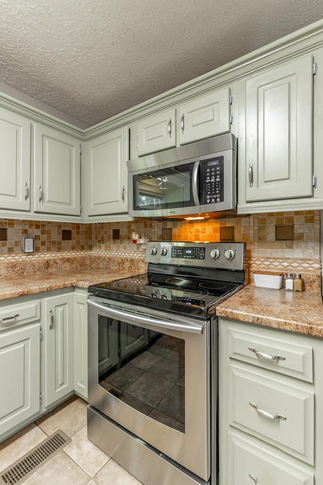 kitchen with appliances with stainless steel finishes, light tile patterned flooring, a textured ceiling, tasteful backsplash, and light countertops