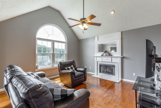 living area with a ceiling fan, lofted ceiling, a high end fireplace, hardwood / wood-style floors, and a textured ceiling