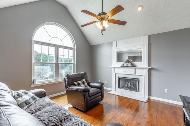 living room with ceiling fan, a premium fireplace, hardwood / wood-style flooring, baseboards, and high vaulted ceiling