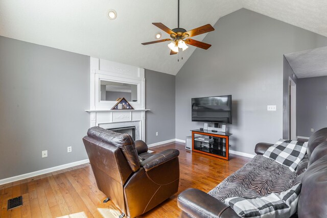 living area featuring ceiling fan, a large fireplace, hardwood / wood-style flooring, baseboards, and high vaulted ceiling
