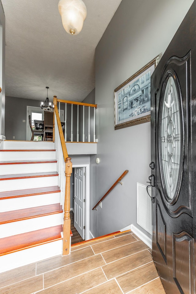 foyer entrance featuring wood finish floors, a chandelier, and stairway
