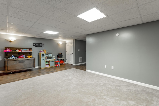 finished below grade area with baseboards, carpet flooring, a paneled ceiling, and wood finished floors