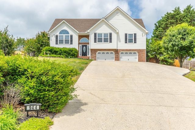 bi-level home with an attached garage, brick siding, and driveway