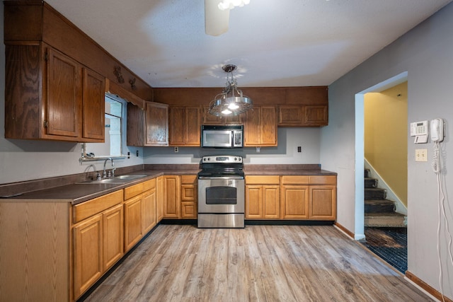 1002 Gillespie Rd, Chattanooga, TN 37411 - kitchen with stainless steel appliances, dark countertops, light wood-style floors, hanging light fixtures, and brown cabinetry