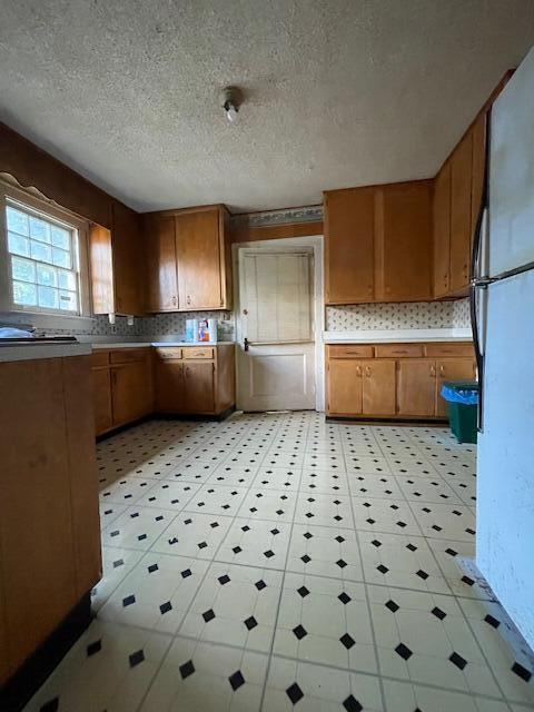 4908 13th Ave, Chattanooga, TN 37407 - kitchen featuring freestanding refrigerator, brown cabinetry, backsplash, and a textured ceiling