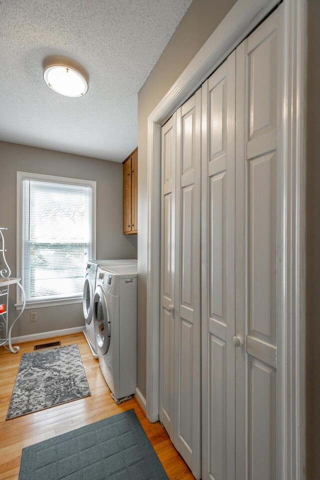 821 Ravine Rd, Signal Mountain, TN 37377 - laundry room with washer and dryer, light wood-type flooring, cabinet space, a textured ceiling, and baseboards