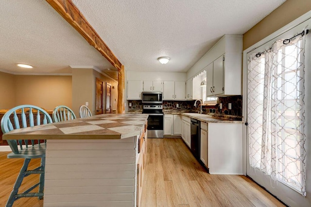 2049 Saunders Rd, Ringgold, GA 30736 - kitchen featuring appliances with stainless steel finishes, a textured ceiling, white cabinetry, light wood finished floors, and a kitchen bar