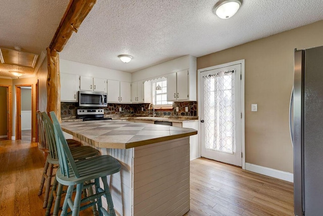 2049 Saunders Rd, Ringgold, GA 30736 - kitchen featuring stainless steel appliances, tile countertops, tasteful backsplash, white cabinets, and light wood-type flooring