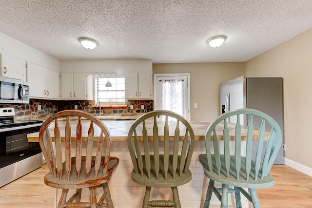 2049 Saunders Rd, Ringgold, GA 30736 - kitchen with stainless steel appliances, light wood-style floors, a breakfast bar area, backsplash, and a textured ceiling