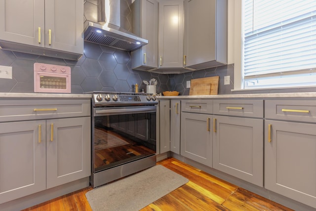 2104 Oak St, Chattanooga, TN 37404 - kitchen featuring wall chimney exhaust hood, gray cabinetry, stainless steel range with electric stovetop, light wood finished floors, and light countertops
