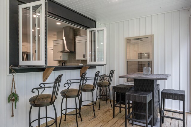 8331 Troubadour Way, Ooltewah, TN 37363 - kitchen with dark countertops, wall chimney range hood, glass insert cabinets, a breakfast bar area, and light wood-style floors
